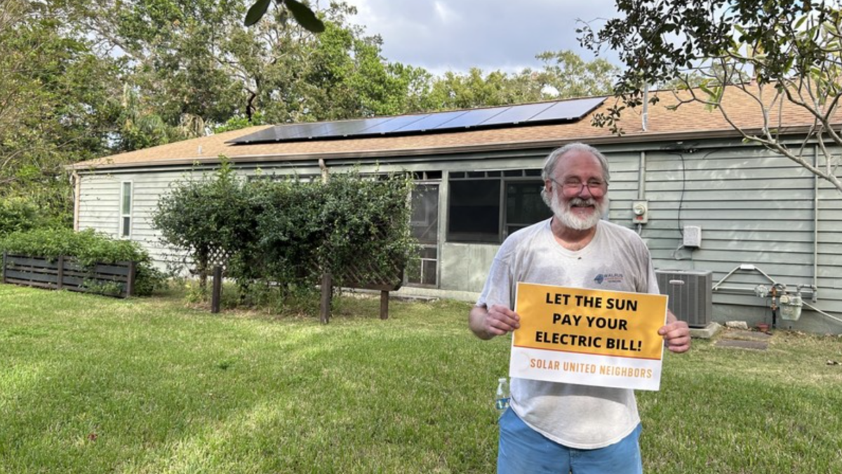 Florida homeowner with sign supporting solar in front of their solar home.